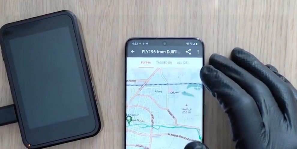 A gloved forensic examiner views drone flight path data on a mobile device during a UAV examination.